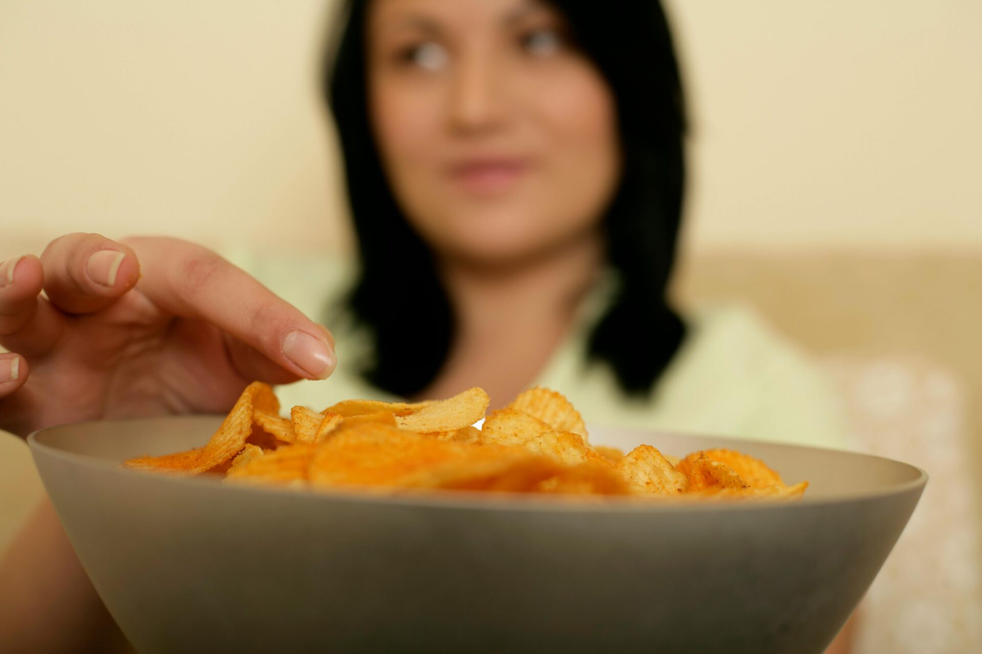 A woman reaching for a bowl full of crispy potato chips, capturing a moment of indulgence.